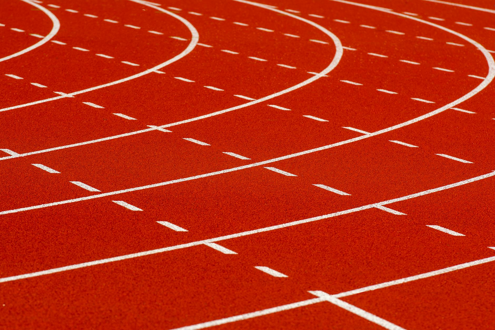 Close-up view of a curved red running track with dashed white lines for athletic sports.