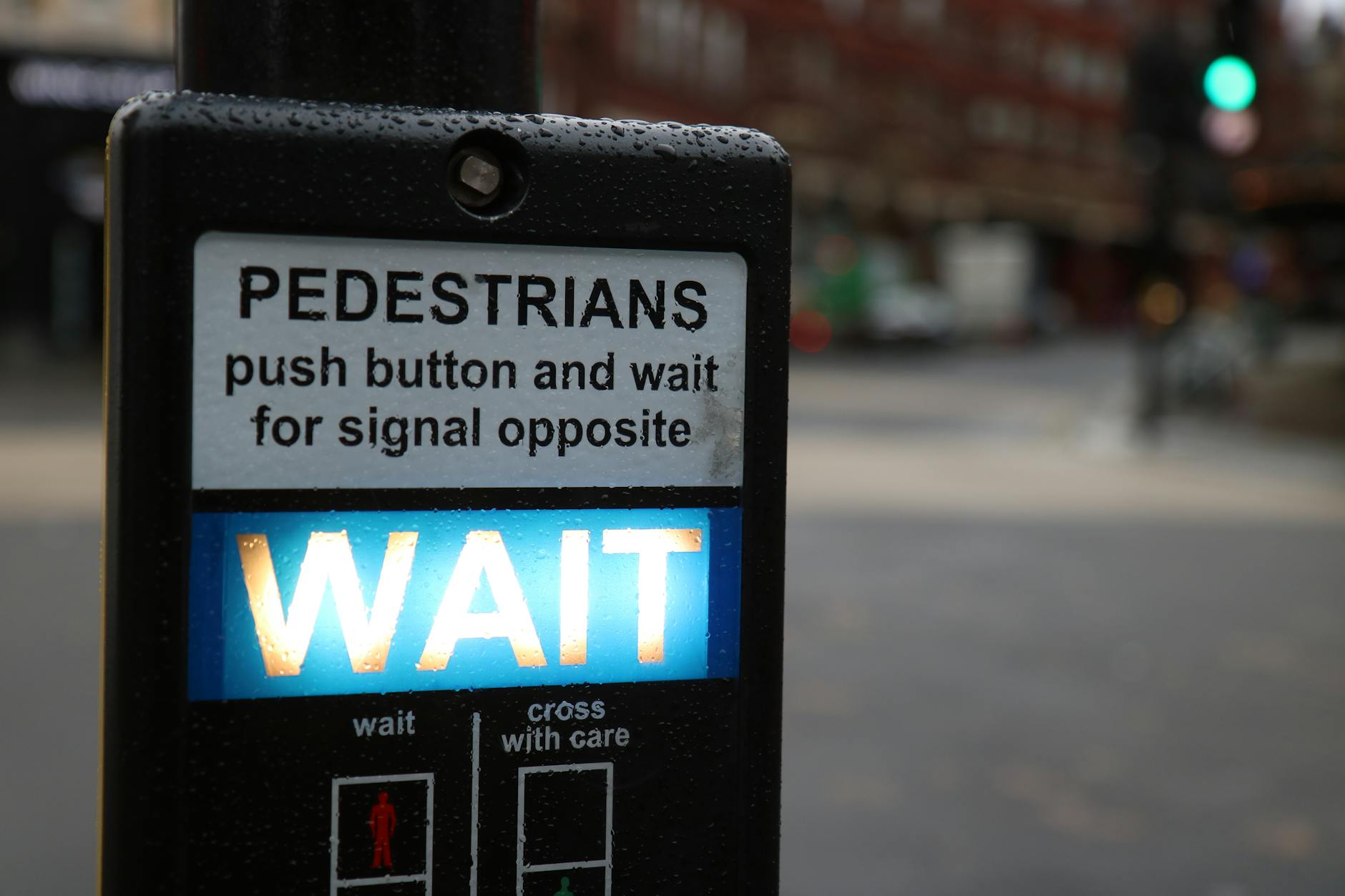 Close-up of a pedestrian crossing button with 'Wait' sign in a rainy London street.