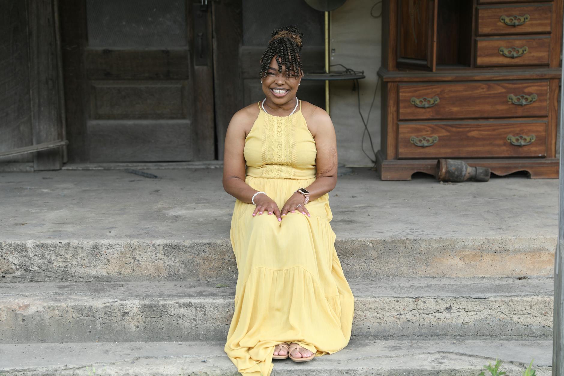 Black woman in a yellow dress sitting on porch steps with a warm smile in Louisiana.