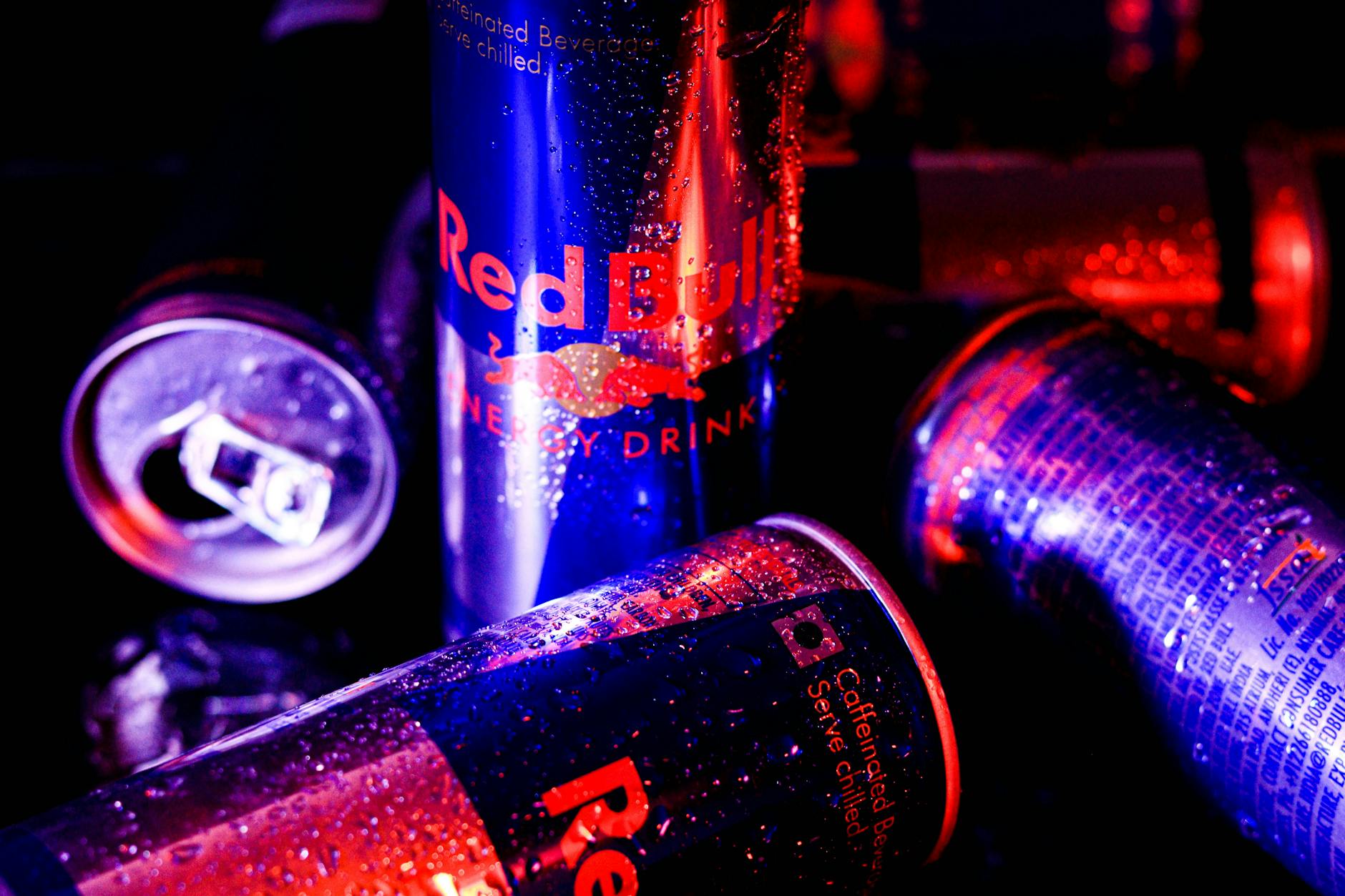 Dynamic image of Red Bull energy drink cans with water droplets in colorful lighting.
