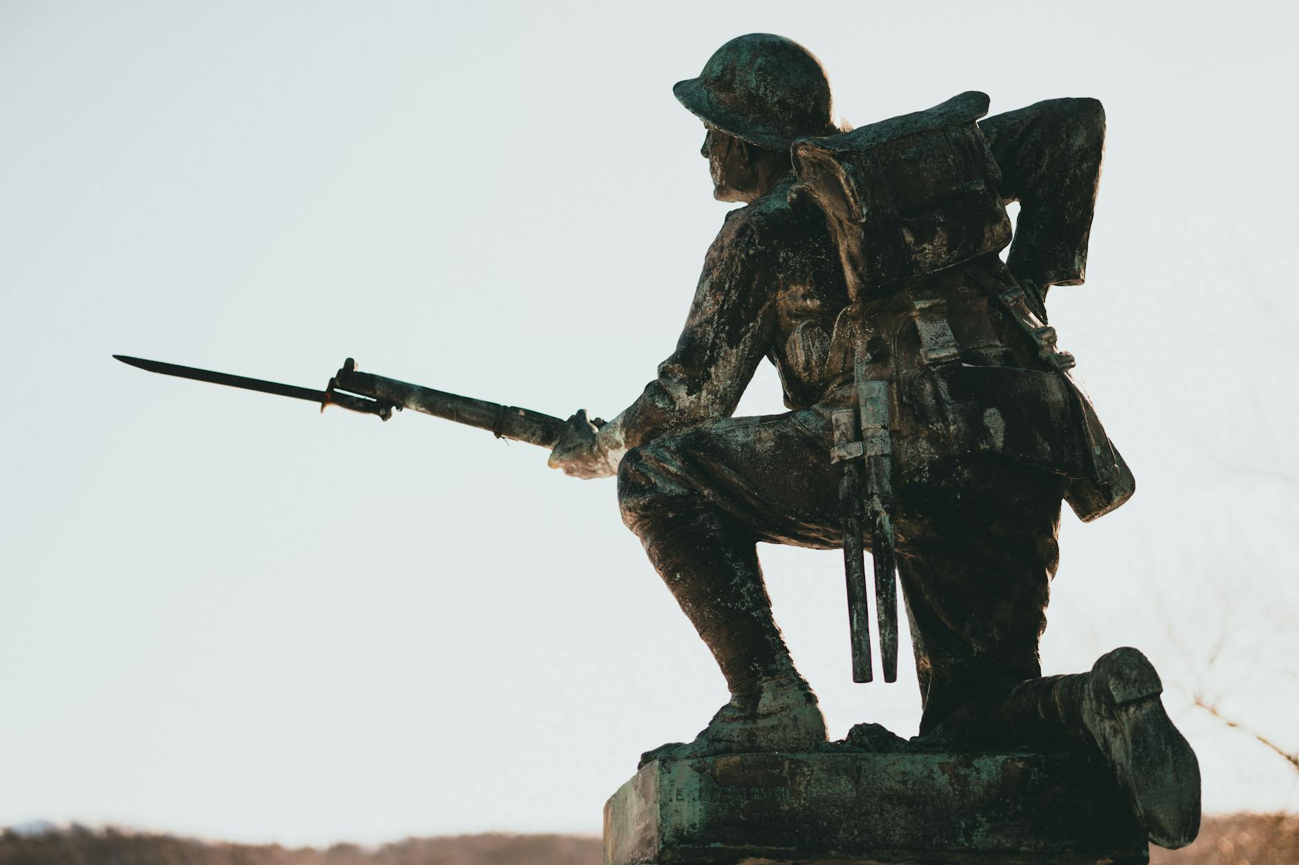 Bronze soldier statue with bayonet, symbolizing military history and valor in sunlight.